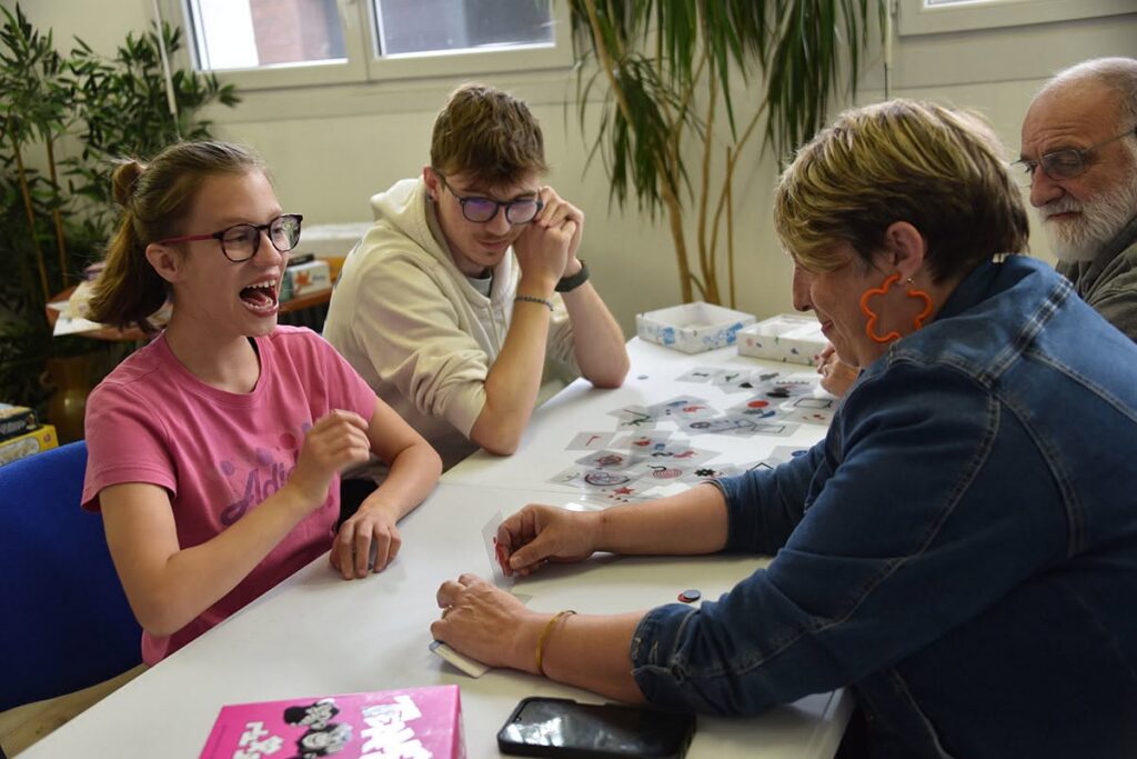 Une petite fille rit pendant une sessions de jeu de société avec sa mère et son frère.
